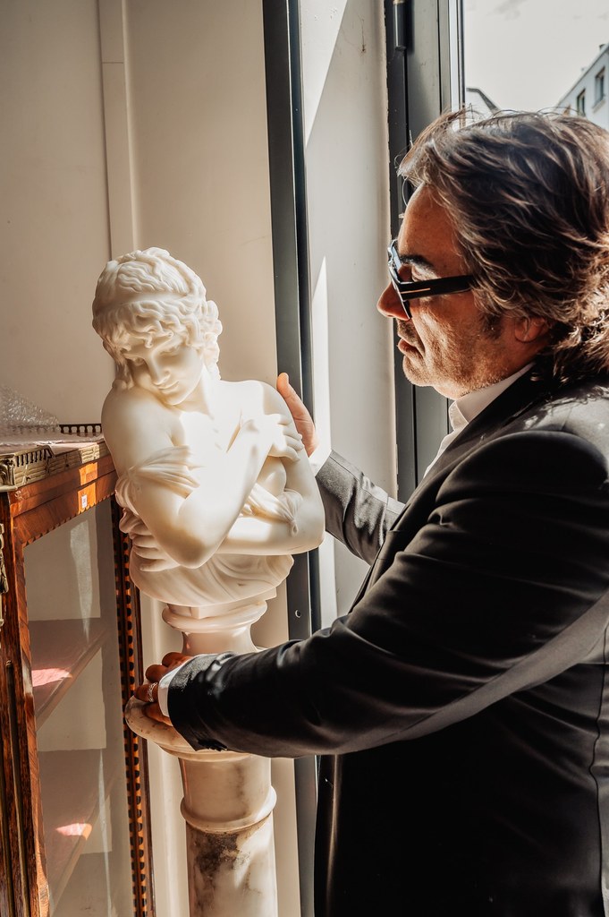 Éric Benhamou examine un buste en marbre près d'une fenêtre