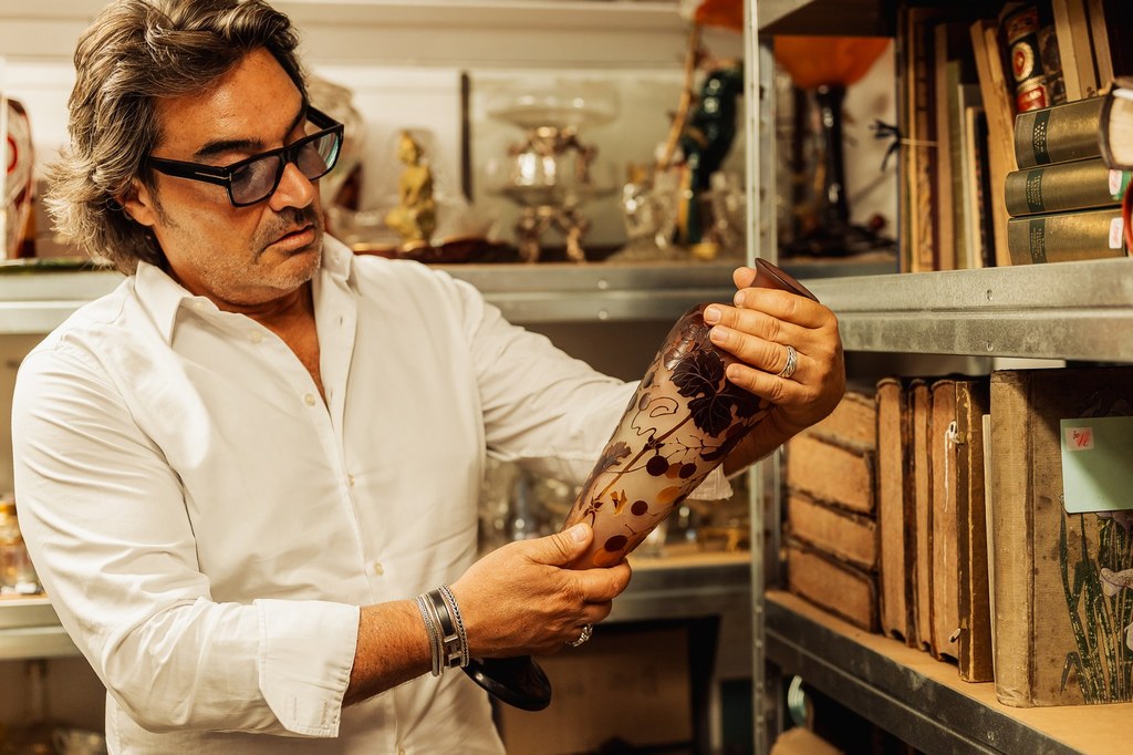 Éric Benhamou examine un vase en pâte de verre devant une bibliothèque