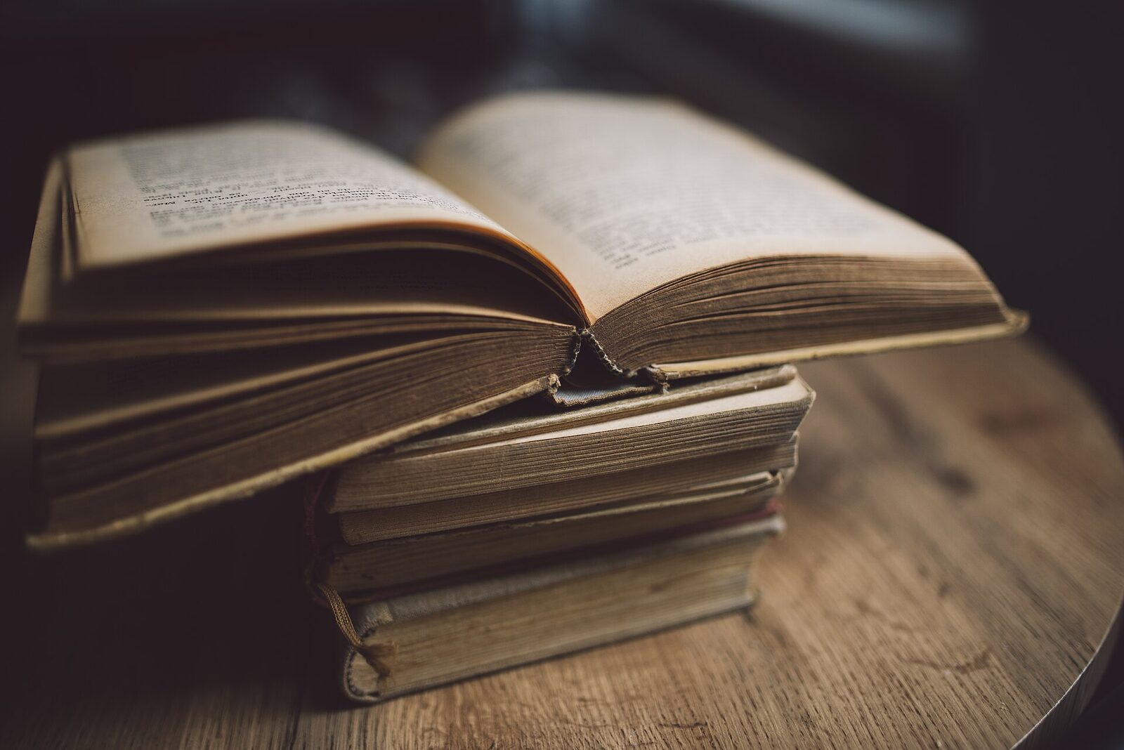 Livre ancien ouvert, posé sur une pile de volumes reliés sur une table en bois